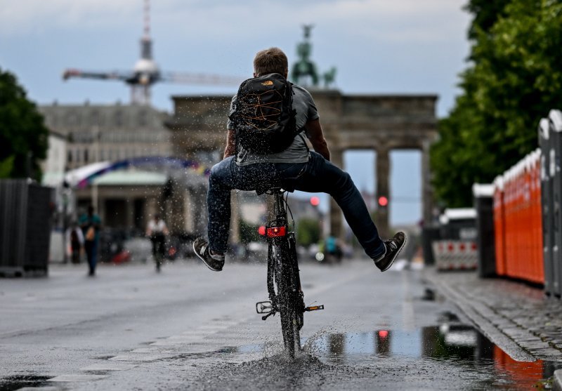 Biciklist vozi kroz lokvuu vode ispred Brandenburških vrata u Berlinu nakon oluje s kišom.