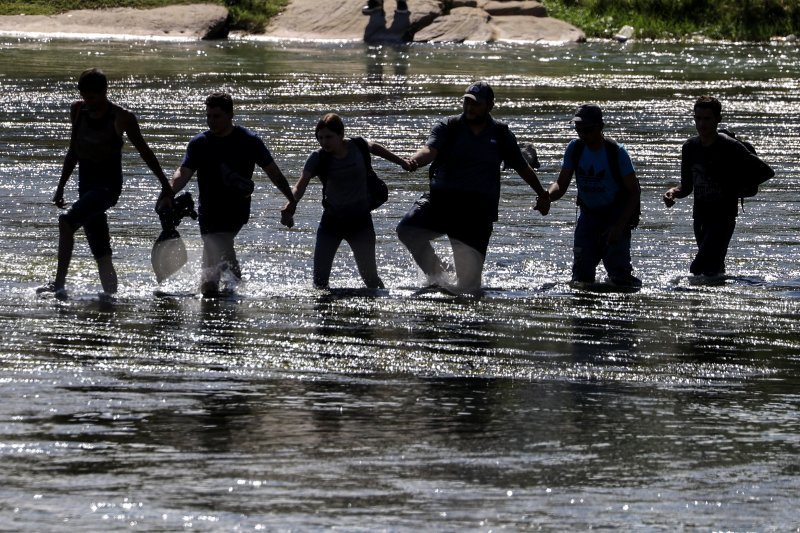 Migranti se drže za ruke dok prelaze rijeku Rio Grande u teksaškom gradu Eagle Pass u kojem je gradonačelnik proglasio stanje lokalne katastrofe zbog tisuća migranata koji su prešli rijeku i došli u grad..