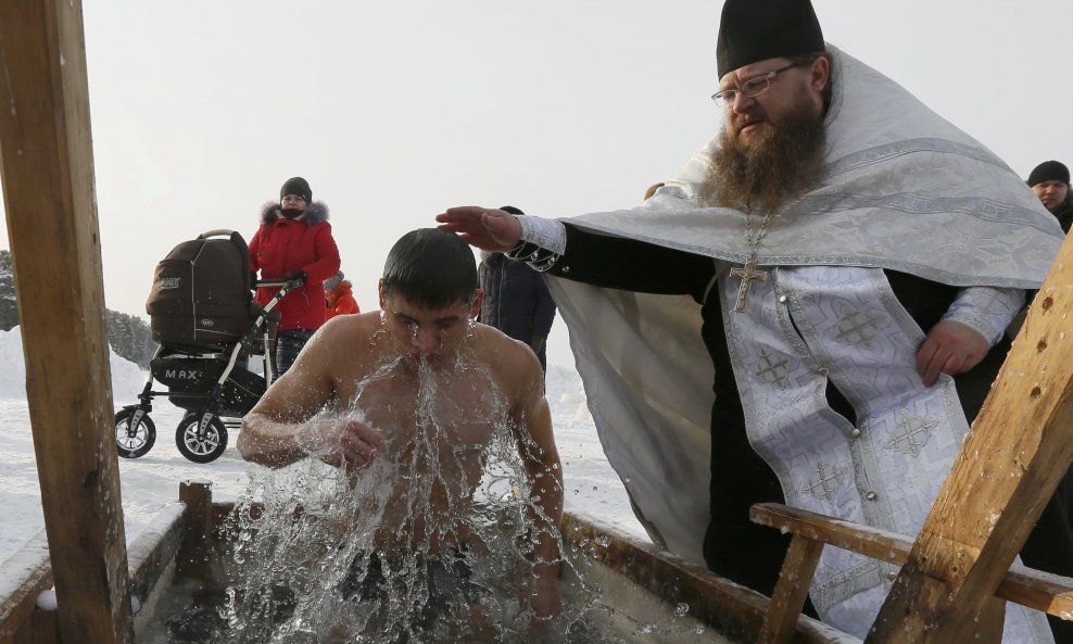 Priest Sergei Ryzhov pushes a man into an ice hole in the frozen Buzim lake during Orthodox Epiphany celebrations, with the air temperature at about minus 18 degrees Celsius (minus 0.4 degrees Fahrenheit), near the village of Sukhobuzimskoye, north of Kra