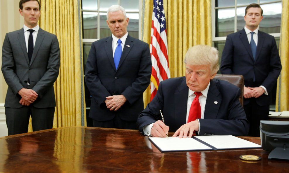 U.S. President Donald Trump, flanked by Senior Advisor Jared Kushner (standing, L-R), Vice President Mike Pence and Staff Secretary Rob Porter welcomes reporters into the Oval Office for him to sign his first executive orders at the White House in Washing