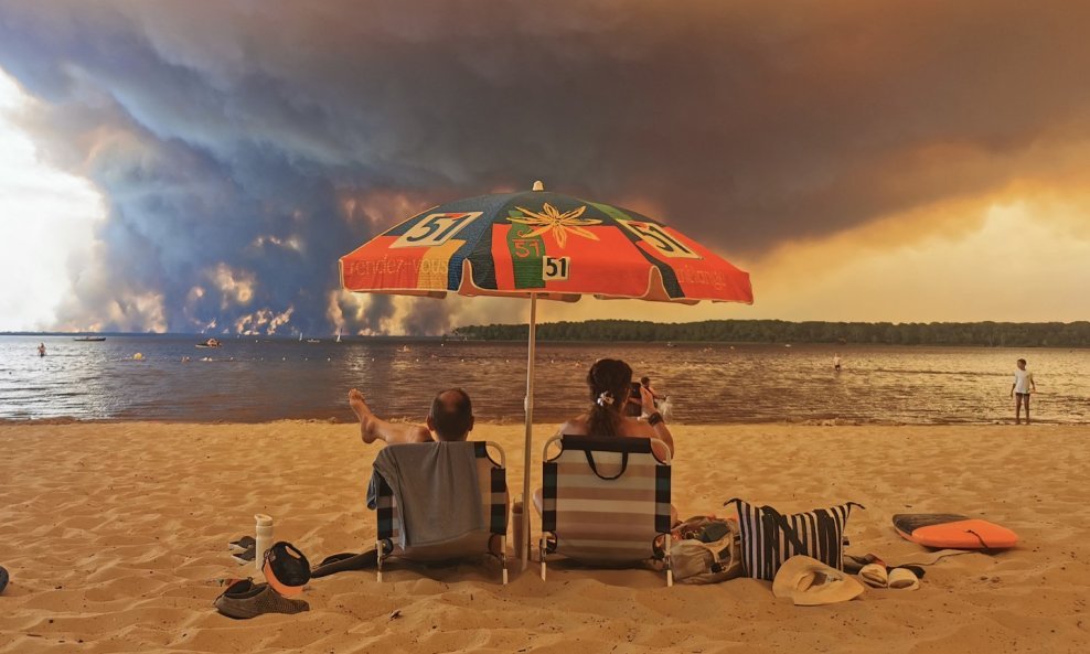 Turisti pod suncobranom promatraju požar i oblak dima